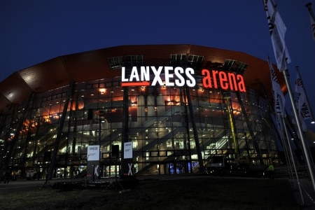 Am Abend leuchtet die Glasfassade der Lanxess Arena Köln und man kann gut die Treppenaufgänge zu den einzelnen Rängen erkennen