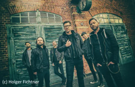 Die Band FIDDLER'S GREEN steht vor einem alten Gebäude alle Musiker sind in schwarz gekleidet