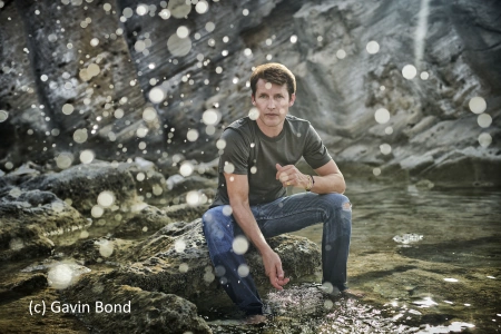 Der Musiker James Blunt sitzt auf einem Stein in einem Fluß