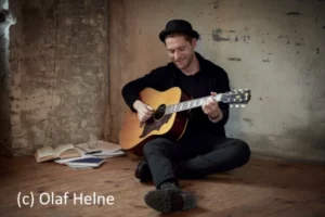 Johannes Oerding spielt auf dem Boden sitzend Gitarre, auf dem Kopf trägt er einen Hut