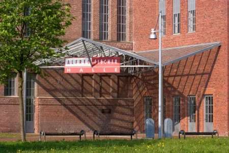 Der überdachte Eingangsbereich der Alfred Fischer Halle in Hamm, davor stehen Bänke und eine grüne Wiese