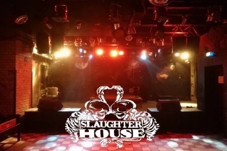 Die Bühne des Slaughterhouse Berlin in buntes Licht getaucht und das Logo der Location