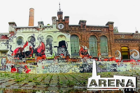 Die mit Graffiti besprühte Aussenfassade der Arena Wien, davor mit Gras bewachsenes Kopfsteinpflaster