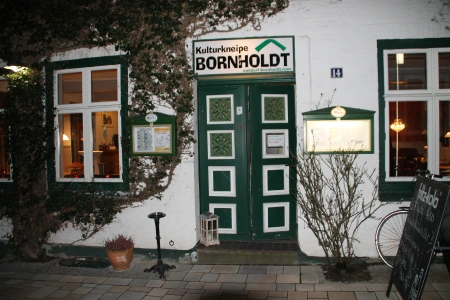 Vor der grün weißen Eingangstür des Bornholdt Meldorf befindet sich eine Stufe. Die Wand ist mit Efeu bewachsen
