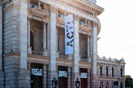 Die Aussenfassade des Burgtheater Wien mit einer weißen Flagge und der Aufschrift ACT! Das Bild stammt von ©studioVIE