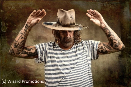 Der Sänger und Songschreiber Donavon Frankenreiter hebt die Hände, trägt einen Hut und ein gestreiftes T-Shirt