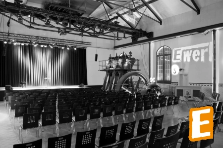Der bestuhlte Innenraum des E-Werk Eschwege. Mit dem Blick auf die Bühne und einer alten Maschine.