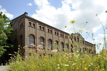 Sag es durch die Blume oder in diesem Fall durch eine Blumenwiese vor der Maschinenhalle Zweckel Gladbeck fotografiert. Die Fassade der Maschinenhalle in rotbraunem Backstein mit hohen Bogenfenstern