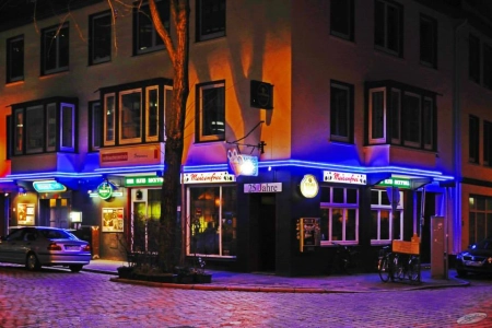 Die leuchtende Neonfassade des Meisenfrei Bremen. Davor die Straße und einige geparkte Autos