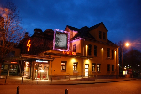 In der Nacht strahlt das E-Werk Erlangen und der charakteristische Blitz an der Seite des Gebäudes.