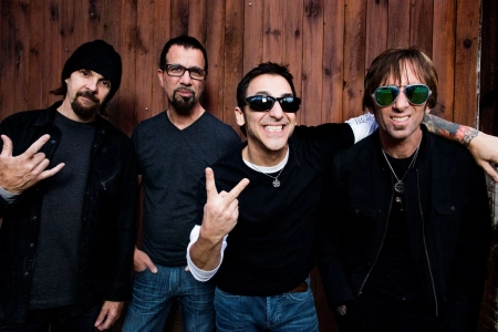 Die vier Mitglieder der Band Godsmack lächeln in die Kamera. Der Sänger zeigt das Viktory Zeichen und ein anderes Bandmitglied die Pommesgabel