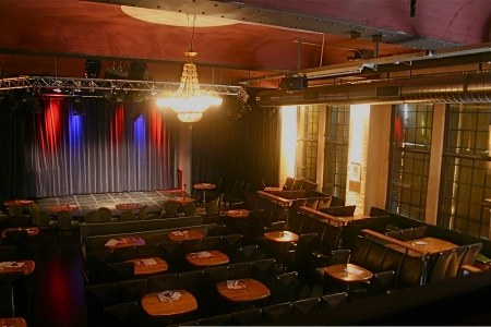Der Innenraum der Käs Frankfurt ist mit Stühlen und Tischen ausgeestattet. Der Blick ist direkt auf die Bühne gerichtet.