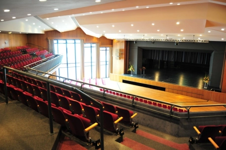 Von der Empore der Stadthalle Limburg hat man einen großartigen Blick auf die Bühne und den darunter liegenden Saal. Die Sitzplätze gleichen klappbaren Kinosesseln mit rotem Posterstoff.