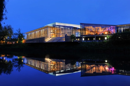 Die Tuttlinger Hallen spiegeln sich in der Dämmerung im Wasser.