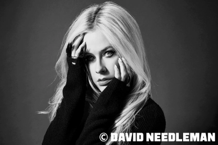 Die kanadische Sängerin Avril Lavigne, sie hält sich fast schüchtern die Hände vor das Gesicht. Das Bild ist in Schwarz Weiß gehalten
