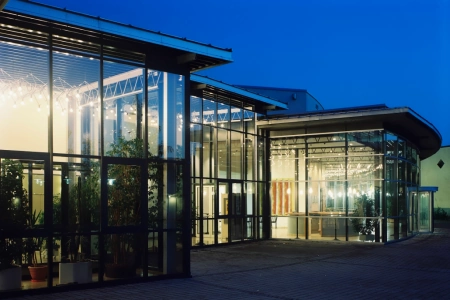 Am Abend leuchten die Lampen im Inneren des Haus der Kultur Waldkraiburg durch die Glasfront. Sie erhellen den Eingangsbereich und den Vorplatz der Location.