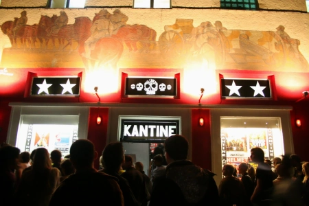 Spät am Abend stehen die Gäste vor dem Eingang zur Kantine Augsburg. Die Schilder beleuchten die Aussenfassade der Location