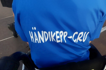Auf dem Shirt eines BUDDIES auf der Wattolümpiade Brunsbüttel im Rollstuhl steht Händikepp-Cru