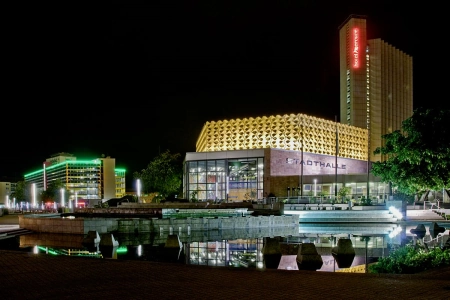 Das Gebäude der Stadthalle Chemnitz leuchtet bei Nacht. Die Glasfassade erstrahlt sehr hell und von weitem sichtbar