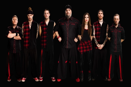 Die sieben Bandmitglieder von Russkaja stehen in einer Reihe nebeneinander. Es sind sechs Männer und eine Frau. Alle tragen rot-schwarze Kleidung.