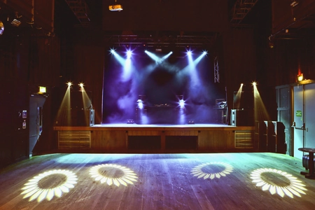 The empty stage of the Button Factory Dublin is illuminated by blue lights. The space in front of it is at ground level.