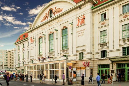 Das Konzerthaus Wien ist ein Bau im klassischen Stil. Die weiße Fassade mit den aufgesetzten Bögen ist beeindruckend. Auf dem Gehsteig sind einige Menschen unterwegs.