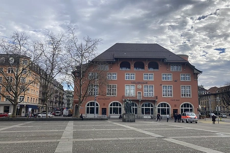 Über den Parkplatz geht es direkt zum Volkshaus Zürich. Die Fassade wurde neu in rot gestaltet davor steht ein Krankenwagen und einige Personen.
