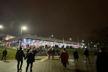 Die hell erleuchtete Stadthalle Rostock bei Nacht mit dem auf den Eingang zugehenenden Gästen.